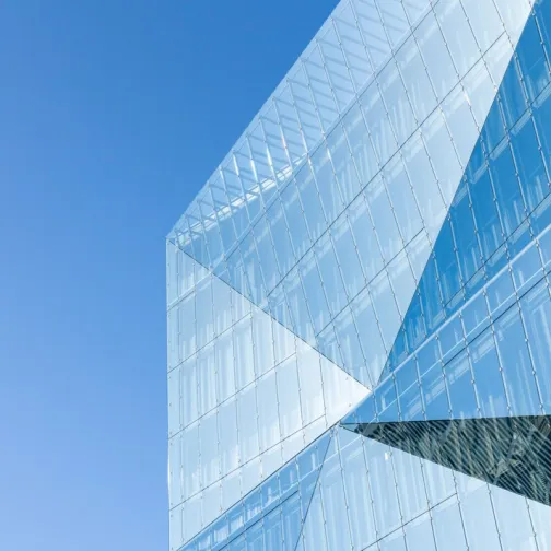 Modern glass building with angular design against a clear blue sky.